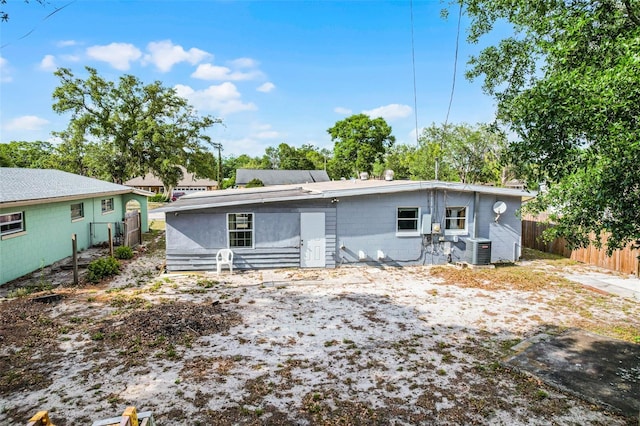 rear view of property featuring central AC unit, concrete block siding, and fence