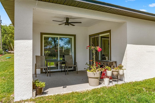 property entrance with a patio, stucco siding, a ceiling fan, and a lawn
