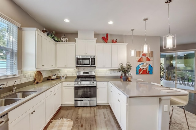 kitchen with a sink, appliances with stainless steel finishes, a peninsula, white cabinetry, and light wood-style flooring