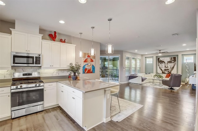 kitchen featuring open floor plan, ceiling fan, appliances with stainless steel finishes, a peninsula, and decorative backsplash