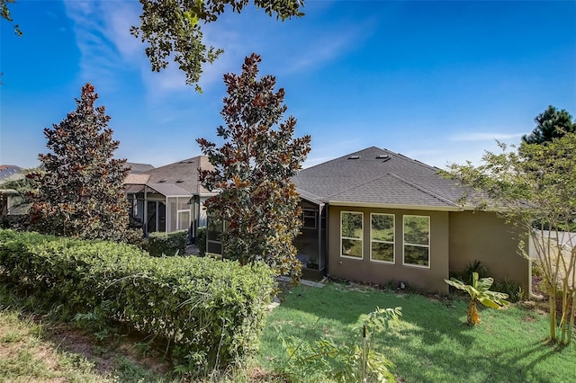 back of property with a yard, roof with shingles, and stucco siding