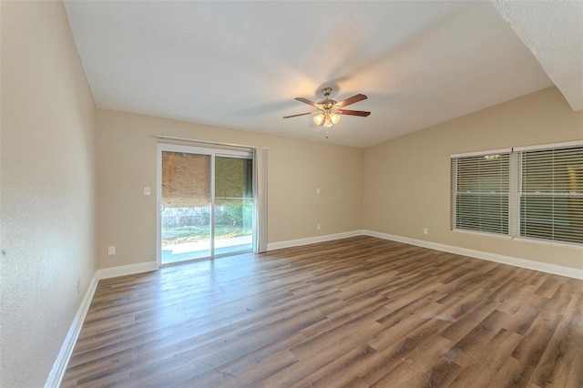 empty room with ceiling fan, wood finished floors, vaulted ceiling, and baseboards