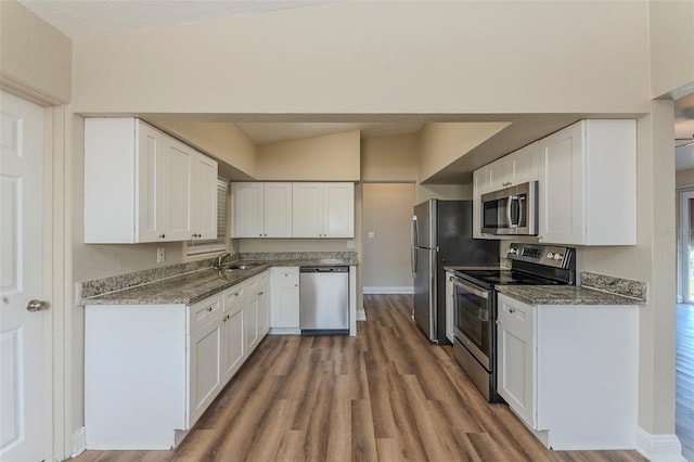 kitchen featuring a sink, appliances with stainless steel finishes, white cabinetry, wood finished floors, and stone countertops