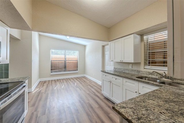 kitchen featuring light wood-type flooring, vaulted ceiling, white cabinets, dark stone counters, and a sink