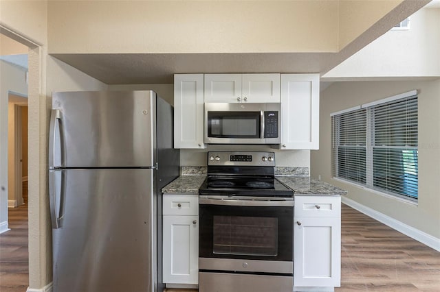 kitchen with stone counters, white cabinetry, wood finished floors, stainless steel appliances, and baseboards