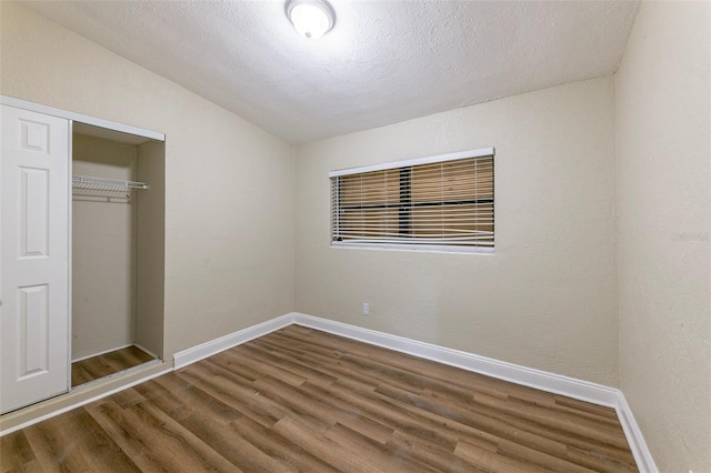 unfurnished bedroom featuring wood finished floors, baseboards, a closet, and vaulted ceiling