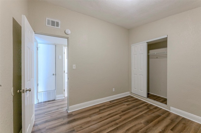unfurnished bedroom featuring a closet, visible vents, baseboards, and wood finished floors