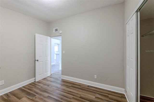 unfurnished bedroom with wood finished floors, baseboards, a closet, and visible vents
