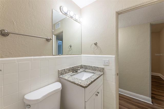 half bath featuring vanity, visible vents, wood finished floors, tile walls, and a textured wall