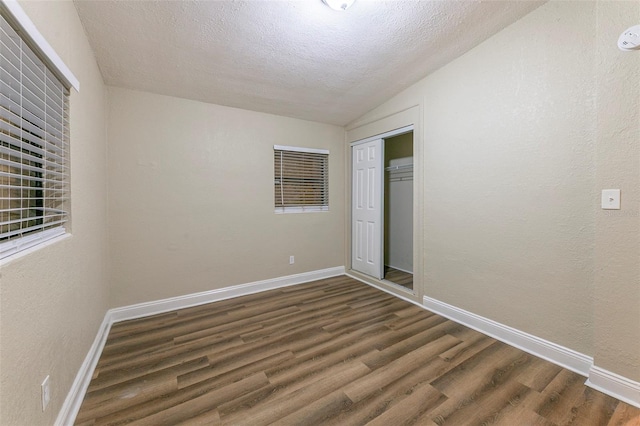 spare room featuring lofted ceiling, baseboards, a textured ceiling, and wood finished floors