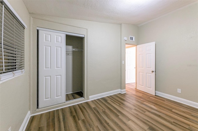 unfurnished bedroom featuring a textured ceiling, wood finished floors, a closet, and baseboards