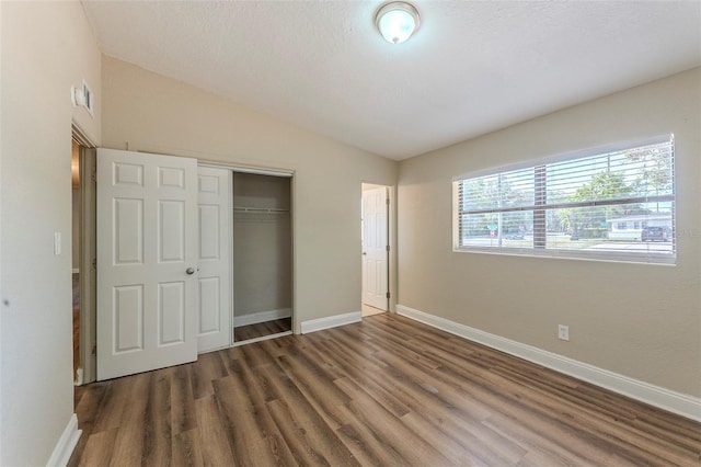 unfurnished bedroom with a closet, baseboards, visible vents, lofted ceiling, and wood finished floors
