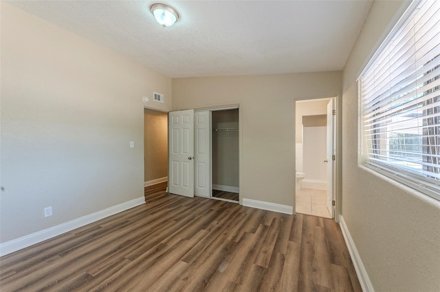 unfurnished bedroom with a closet, visible vents, wood finished floors, lofted ceiling, and baseboards