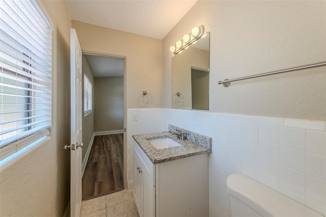 bathroom featuring vanity, tile patterned floors, toilet, wainscoting, and tile walls