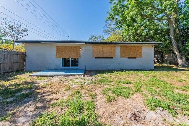rear view of house featuring a yard, concrete block siding, fence, and a patio