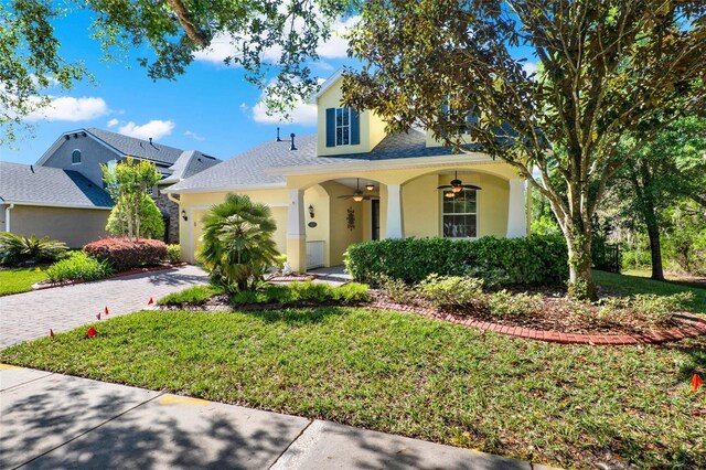 view of front facade with a garage, decorative driveway, a ceiling fan, and a front lawn
