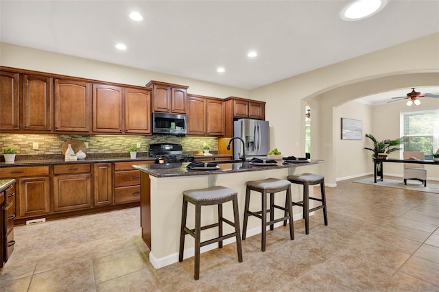 kitchen featuring a kitchen breakfast bar, arched walkways, stainless steel appliances, a center island with sink, and decorative backsplash
