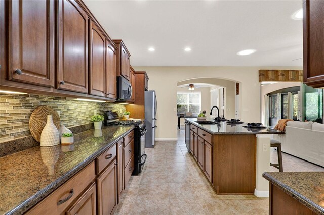 kitchen with a breakfast bar, decorative backsplash, stainless steel appliances, arched walkways, and a sink