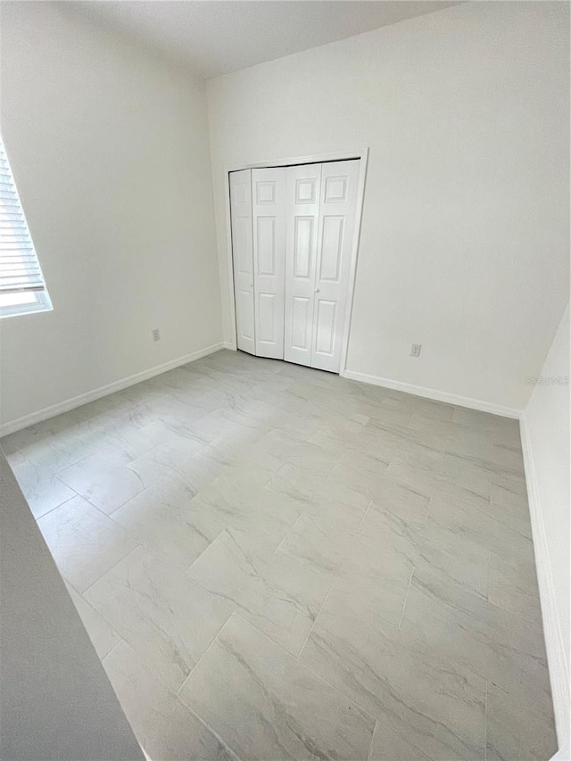 unfurnished bedroom with baseboards, marble finish floor, and a closet