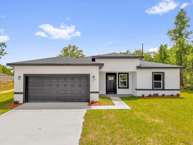prairie-style house with a front yard, an attached garage, stucco siding, driveway, and roof with shingles