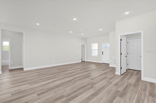 unfurnished living room with a wealth of natural light, recessed lighting, light wood-style flooring, and baseboards