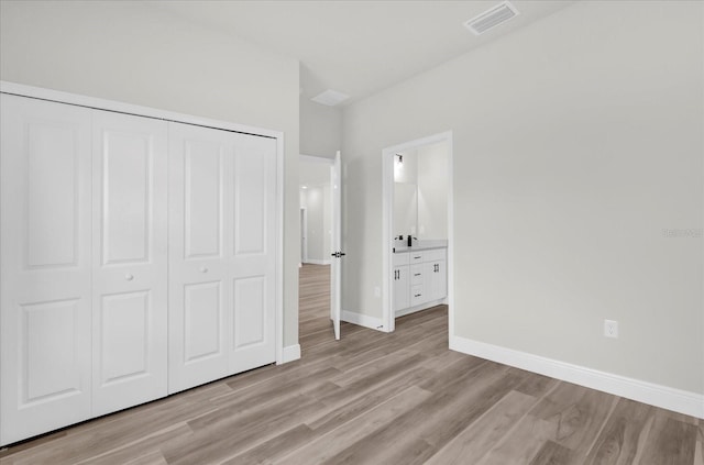 unfurnished bedroom featuring a closet, baseboards, ensuite bath, light wood-style flooring, and visible vents