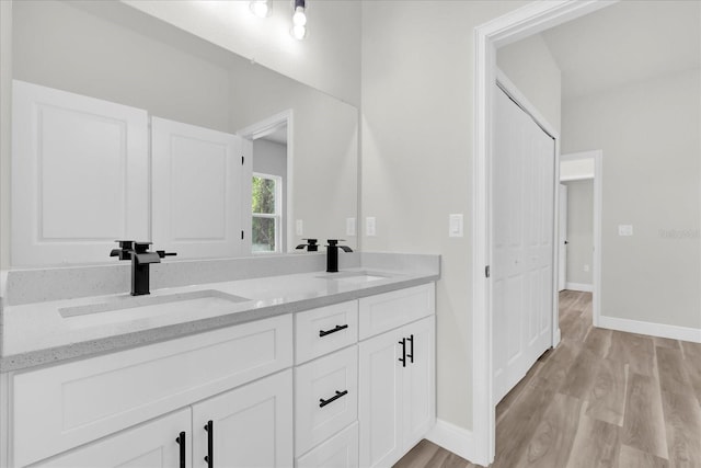 bathroom with wood finished floors, double vanity, a sink, and baseboards