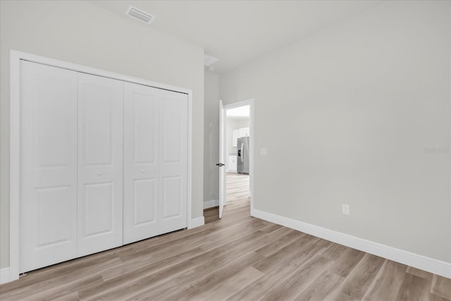 unfurnished bedroom with a closet, baseboards, visible vents, stainless steel refrigerator with ice dispenser, and light wood-type flooring
