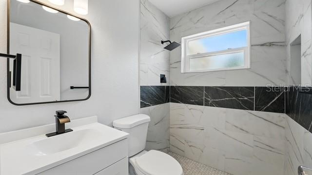 full bath featuring toilet, vanity, and a marble finish shower