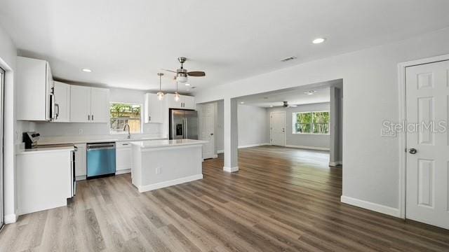 kitchen with ceiling fan, appliances with stainless steel finishes, a kitchen island, and a healthy amount of sunlight