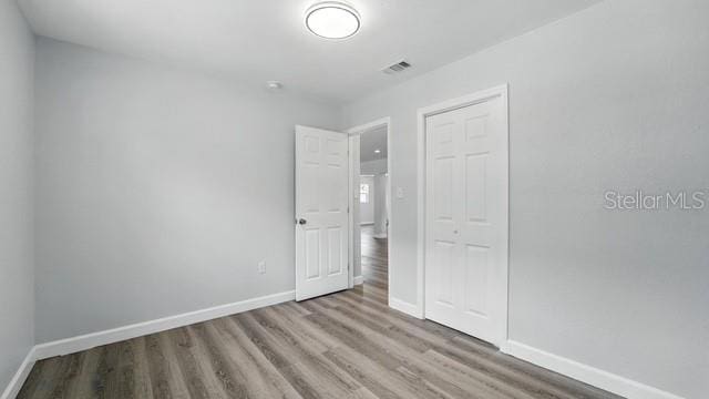 unfurnished bedroom with a closet, wood finished floors, visible vents, and baseboards