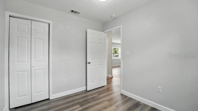 unfurnished bedroom with visible vents, wood finished floors, baseboards, and a closet