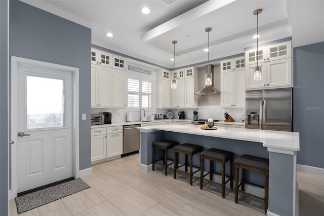 kitchen with wall chimney range hood, a tray ceiling, backsplash, and appliances with stainless steel finishes