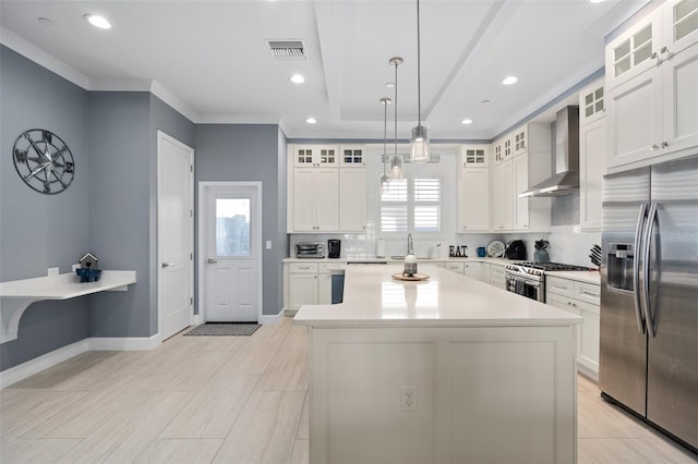 kitchen featuring wall chimney exhaust hood, visible vents, a center island, appliances with stainless steel finishes, and backsplash