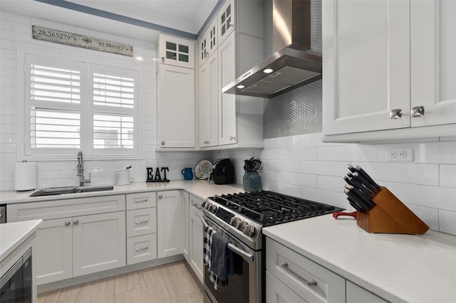 kitchen featuring tasteful backsplash, white cabinets, a sink, wall chimney range hood, and appliances with stainless steel finishes