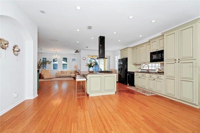kitchen featuring black appliances, open floor plan, light wood-style flooring, and cream cabinets