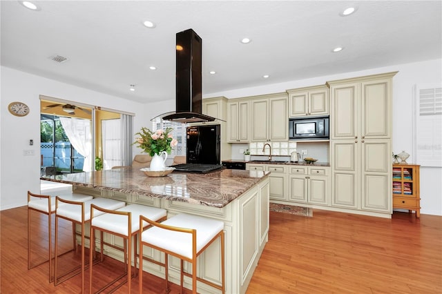 kitchen featuring light wood-type flooring, black appliances, cream cabinetry, a center island, and island exhaust hood