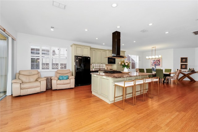 kitchen featuring visible vents, black fridge, island range hood, cream cabinets, and a kitchen island