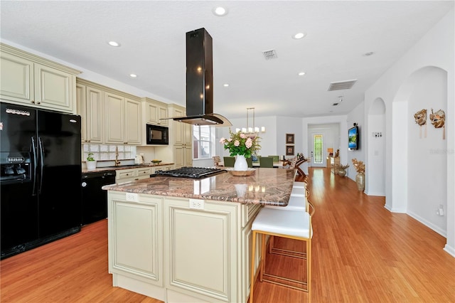 kitchen featuring island range hood, visible vents, black appliances, and cream cabinetry