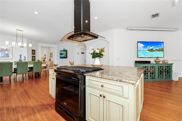 kitchen with visible vents, light wood-type flooring, black range with gas stovetop, island exhaust hood, and cream cabinets