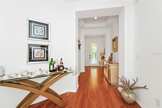 hallway with light wood-style floors, a tray ceiling, and baseboards