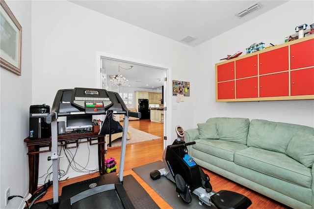 exercise area featuring visible vents, an inviting chandelier, and wood finished floors