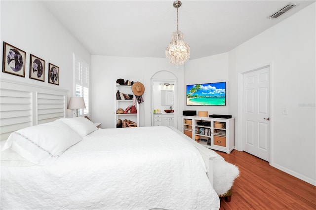 bedroom with visible vents, baseboards, ensuite bathroom, a notable chandelier, and wood finished floors