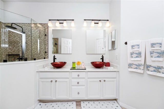 bathroom with tiled shower, double vanity, a sink, and baseboards