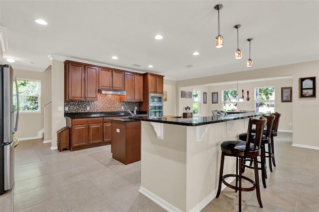 kitchen featuring stainless steel appliances, a large island, baseboards, crown molding, and under cabinet range hood