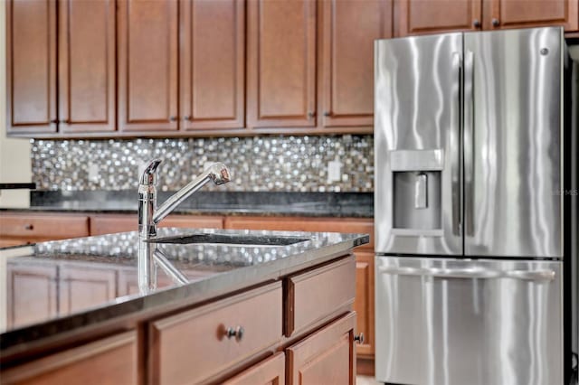 kitchen with dark countertops, tasteful backsplash, a sink, and stainless steel fridge