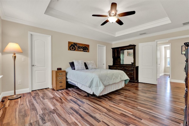 bedroom featuring visible vents, wood finished floors, a tray ceiling, and ornamental molding