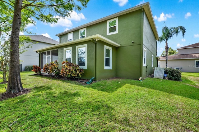 rear view of house featuring a lawn and stucco siding