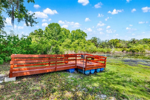 deck featuring a forest view, a lawn, a water view, and fence