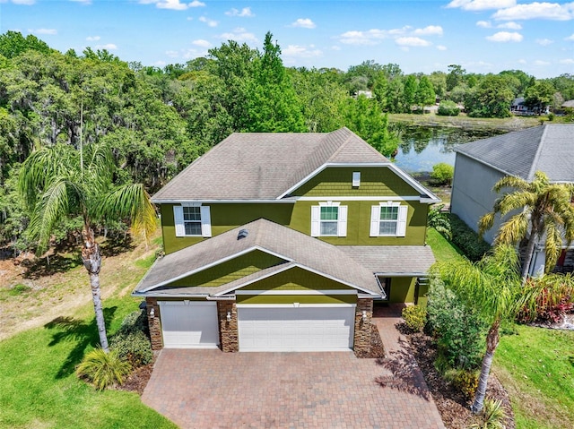 craftsman-style home featuring a water view, a front lawn, an attached garage, stucco siding, and decorative driveway